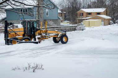Şiddetli bir kar yağışından sonra, bir Motor Grader kar küreme aracı konut alanını temizliyor.
