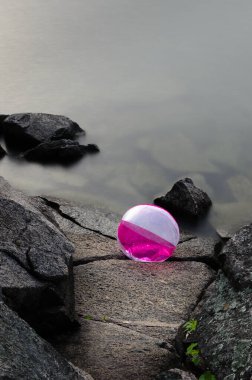 Mor ve beyaz plaj topu suyun kenarındaki dalgalar tarafından kayalara sıkıştı.