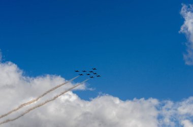 Siluetli dokuz jet savaşçısı bulutlu mavi gökyüzüne karşı buhar izleri oluşturdu.