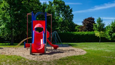 Yazın mavi gökyüzünün altında halka açık bir parkta kırmızı kaydırak ve oyun alanı yapısı.