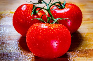 Üç taze domatesli bir grubun ön görüntüsü sarmaşığın üzerinde, ahşap kesme tahtasındaki su damlacıklarıyla kaplı..