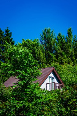 Üzerinde açık mavi gökyüzü olan balkonlu bir ev ağaçların tepesini dürtüyor..