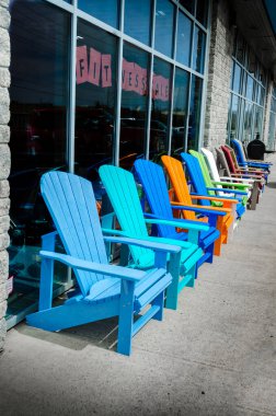 Boş renkli Adirondack sandalyelerin sırası kaldırımda renkli cam bir vitrinin önünde, boş sandalyelerin üstündeki pencerede 