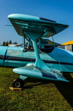 Yakından bakınca, açık mavi bir çift kanatlı uçağın çimlerin üzerine park edilmiş bir hangar seti..