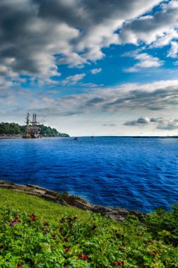 İki uzun gemi Brockville, Ontario yakınlarında korunan bir limana demirlediler. St. Lawrence nehri üzerinde bir park ve önü mavi bir su ve mavi gökyüzü ile dolu.