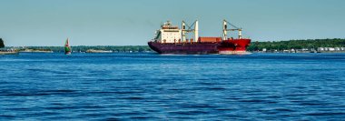 St. Lawrence Seaway 'de, gökyüzü açık bir yelkenlinin yanında, yalnız ve paslı bir geminin panoraması..