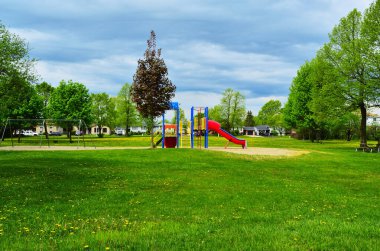 Fırtınalı bir gökyüzünün altında bahar karahindibaları olan yerleşim yerindeki bir parkın renkli bir oyun alanı manzarası