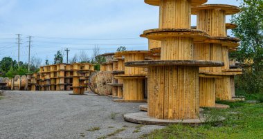 Boş sanayi tipi tahta tel makaraların panoraması mavi gökyüzünün altında hidroelektrik kablolarının yanında istiflenmiş.