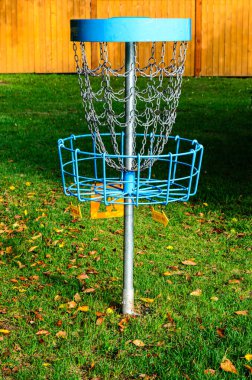 Güneşli bir sonbahar sabahında arka planda ahşap bir çitle çimenlikte bir disk golf hedefinin yakın çekimi..