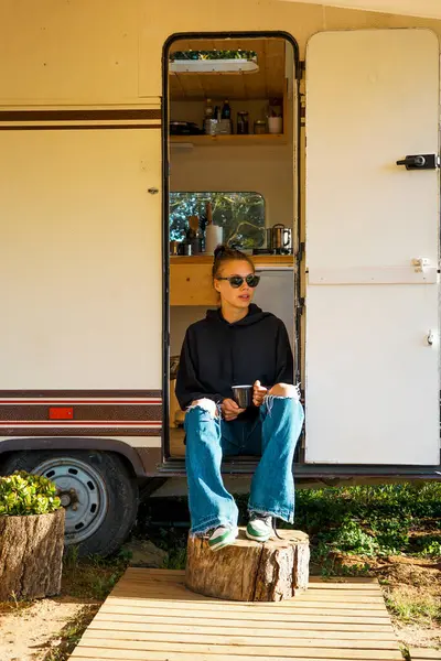 Bir kız gün batımında kafasında çay şapkası olan bir karavanın yanında oturur. Kız kahve içiyor. Gezgin.