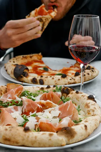 Genç moda eğlence adamı bir bardak şarapla pizza yiyor. Güneş gözlüğü, harika tasasız bir gün, şehir tarzı.