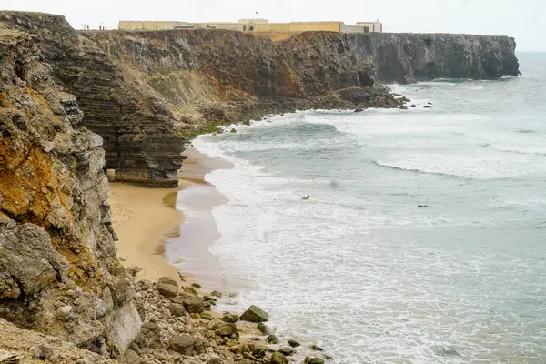 Okyanusta sörfçüler. Cape Sagres, Algarve, Portekiz 'deki Praia do Tonel (Tonel plajı) panorama manzarası. Praia Do Tonel, Alentejo, Portekiz plajı. Praia Do Tonel sahilinde okyanus dalgaları. Sagres Kalesinden Görünüm.