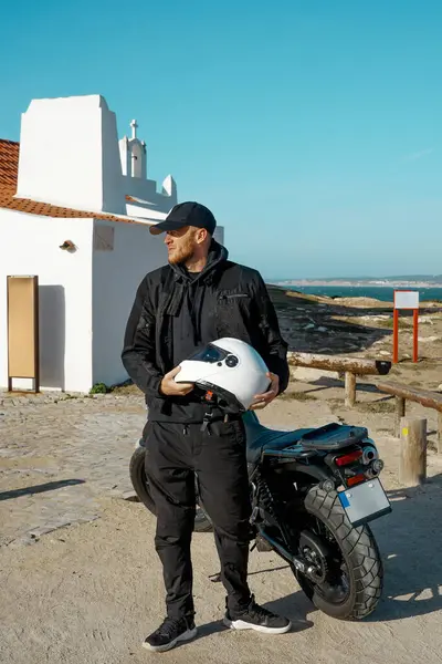 Erkek motorcu elinde bir motosiklet kaskı ve uçurumlarda havalı bir Honda motosikleti tutuyor, Portekiz, Penis Seyahati, Avrupa 'da tatil, motosikletçi tarzı..