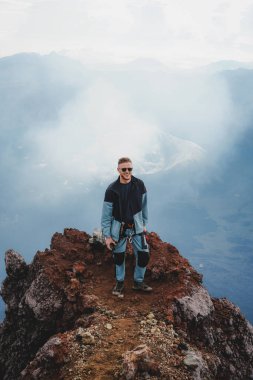 Handsome young men Hiker Standing on Mount Ruang Volcano Summit with Scenic Mountain View clipart