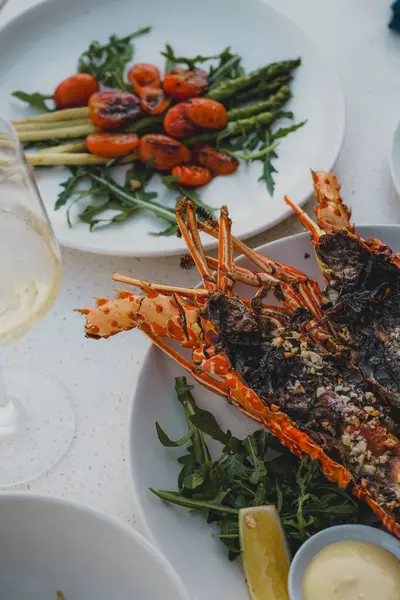 Şık bir sofrada ızgara ıstakoz, kızarmış sebze ve beyaz şarap eşliğinde gurme deniz ürünleri yemeği.