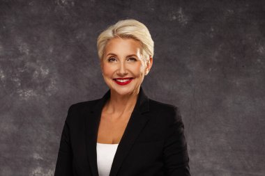 Kısa sarı saçlı, kendine güvenen, şık bir kadın. Makyajlı ve kameraya gülümsüyor. Zarif bir iş kadını. Stüdyo çekimi. Boşluğu kopyala.