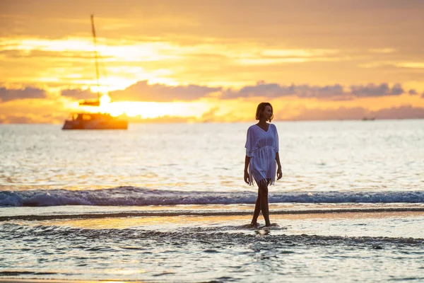 沉着的女人享受着金色的夕阳 在沙滩上散步 背带着帆船 采购产品旅行 生活方式的概念 — 图库照片