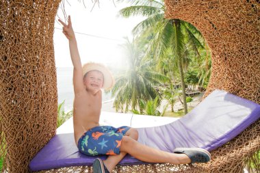 Mutlu altı yaşındaki çocuk güneşli yaz tatilinde eğleniyor, kumsalda dinleniyor, kameraya gülümsüyor. Çocuk barış sembolü gösteriyor. Arka planda avuçlar, 