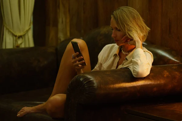 Evdeki Kanepede Oturan Neşeli Sarışın Kadın Akıllı Telefon Kullanıyor Kız — Stok fotoğraf