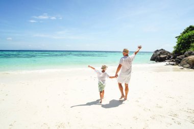 Happy family , dad and son, having fun together at the tropical beach, playing and looking at the blue sea and sky. Summer vibes. Island life. Tourists. 