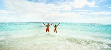 Beach summer vacation photo of happy couple relaxing and having fun on tropical holidays. Playful man and woman in swimwear holding hands. Honey moo