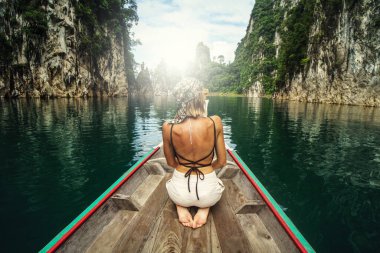 Back View of Young Female Tourist at Longtail Boat over Limestone Cliffs at Cheow Lan Lake. Khao Sok National Park in Thailand, Asia. Tropical vacation. Traveler. Amazing nature