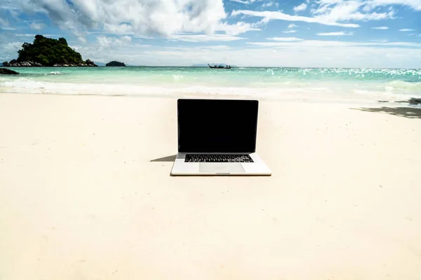 Computer notebook with empty black screen on the sandy tropical beach - digital nomad concept. Business travel.