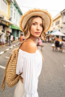 Woman traveler with boho backpack and hat looking at the camera, walking in old town, sightseeing, Thailand, Asia. Tourism. Travel concept.