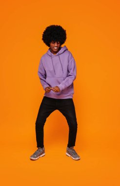 Smiling young african american man isolated on orange studio background posing and dancing. People sincere emotions. Fashionable style. Full length photo