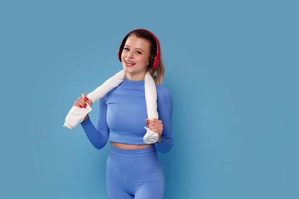 Sport Happy Model. Young Fit Woman Wearing Wireless Headphones Posing Over blue studio pastel Background. A lot of copy space