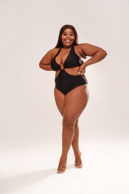 Full length photo Of Curvy Smiling African American Woman posing in black swimsuit. Studio shot. Body positive.  clipart