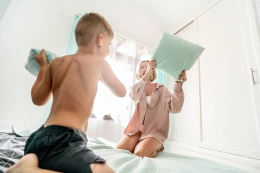 Çok mutlu, mutlu bir anne ve oğlu var. Yatak odasında yastık savaşı oynuyorlar. Komik bir aile aktivitesi. Gerçek insan yaşam tarzı.