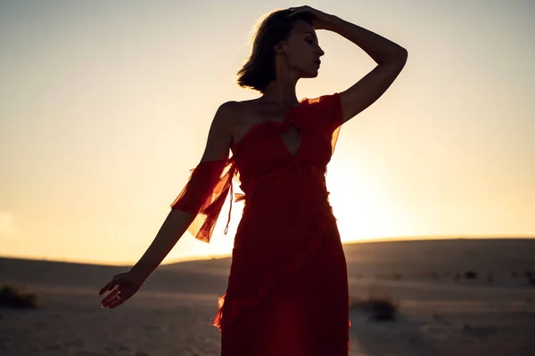 夕日の光で砂漠の中にポーズを赤いドレスを着たロマンチックな女性の肖像画 スペースのコピー — ストック写真