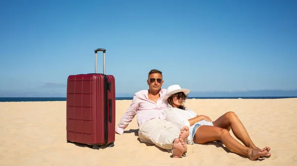 Traveling couple relaxing with suitcases at the beach on a sunny summer day, tired after looking for the good place for sunbathing. A lot of copy space. Tourism