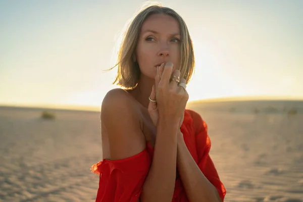 一个穿着红色衣服的浪漫金发女人在金色夕阳西下躺在沙滩上的画像 手上戴着时髦戒指的女孩 — 图库照片