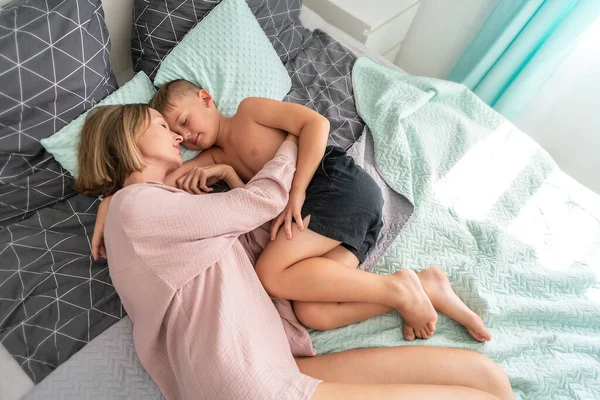 Calm, lovely mother and little boy sleeping together, cuddling. Loving family of two at early morning at home, hugging in bedroom. Childhood and parenthood concep
