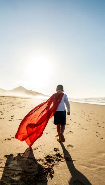 スーパーヒーローの子は 砂の上を歩くと 夕日のビーチ 赤いマスクとケープを着て バックビュー 夏休みのコンセプト コピースペース 子供の力 — ストック写真