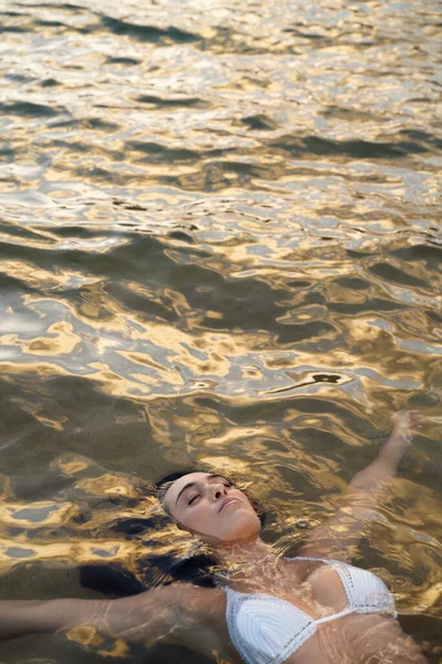 美しい白いビキニの若い女性が海の水の中に横たわっていた 日没黄金の光 落ち着いて穏やかな人々 スペースのコピー — ストック写真