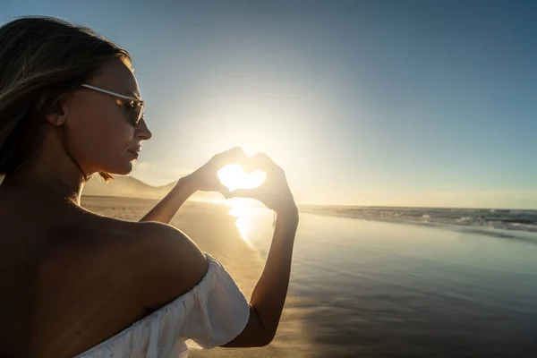 平静的女人手牵手的心形 背景是日落和海洋 暑假和旅行的概念 游手好闲 — 图库照片