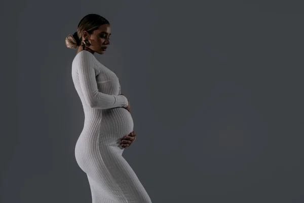 妊娠中の女性の肖像画 白いエレガントなドレス 彼女の腹を受け入れる 妊娠コンセプト たくさんのコピースペース スタジオの背景 プロフィールビュー — ストック写真