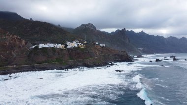 İspanya 'nın Tenerife adasının kuzey kıyısında büyük dalgalarla birlikte vahşi kıyı şeridinin panoramik hava manzarası. Dağlarda küçük bir köy. Seyahat hedefi