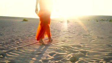 Gün batımında çölde yürüyen kırmızı giysili zarif bir kadın. Fuerteventura Adası.