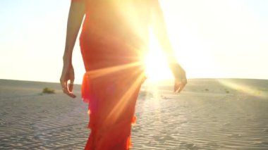 Gün batımında çölde yürüyen kırmızı giysili zarif bir kadın. Fuerteventura Adası.