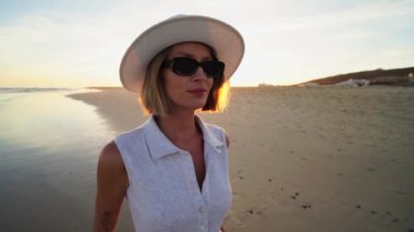 Beyaz şapkalı mutlu kadın gülümsüyor, güzel sahilde günbatımının tadını çıkarıyor. Turist. Seyahat et. Fuerteventura.