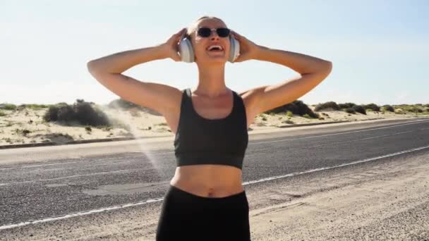 年轻的女人站在海滨大街上 早上慢跑后放松 用白色的手机听音乐 健康的生活方式概念 上午例程 — 图库视频影像