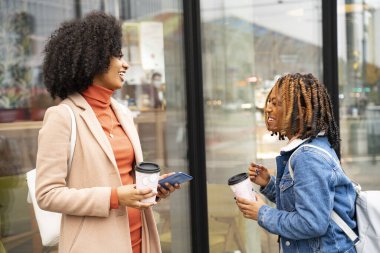 İki güzel Afrikalı kadın arkadaş dışarıda kahve içiyor, gülümsüyor ve konuşuyorlar. Turistler restoranın önünde dinleniyor. Moda kızları..