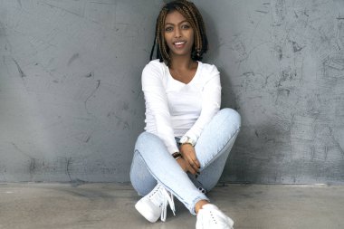 Mutlu, Afro-Amerikalı genç bir kadın yerde oturuyor, gülümsüyor ve kameraya bakıyor..