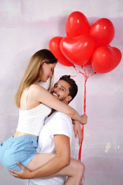 Birbirlerine aşık genç ve güzel bir çift pembe stüdyo arka planında kırmızı kalp şeklinde bir balonla poz veriyorlar. Sevgililer Günü, aşk, ilişki ve gerçek insan duyguları konsepti. Kopyalama alanı.