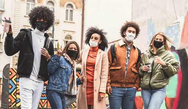 Happy young group of multiethnic friends having fun in the city after quarantine, wearing face mask. Youth millennial generation friendship.