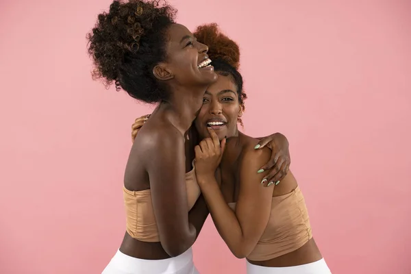 Happy real people relationships. Cheerful african american women friends smiling, having fun together. Pink pastel studio background.
